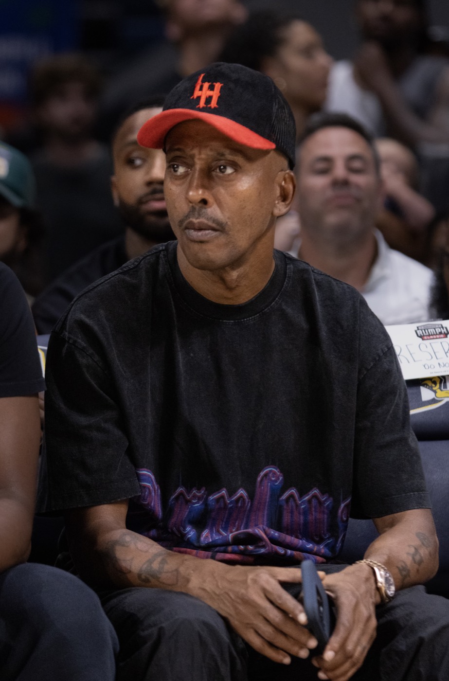 Courtside portrait of a man in a black shirt and red-trim cap