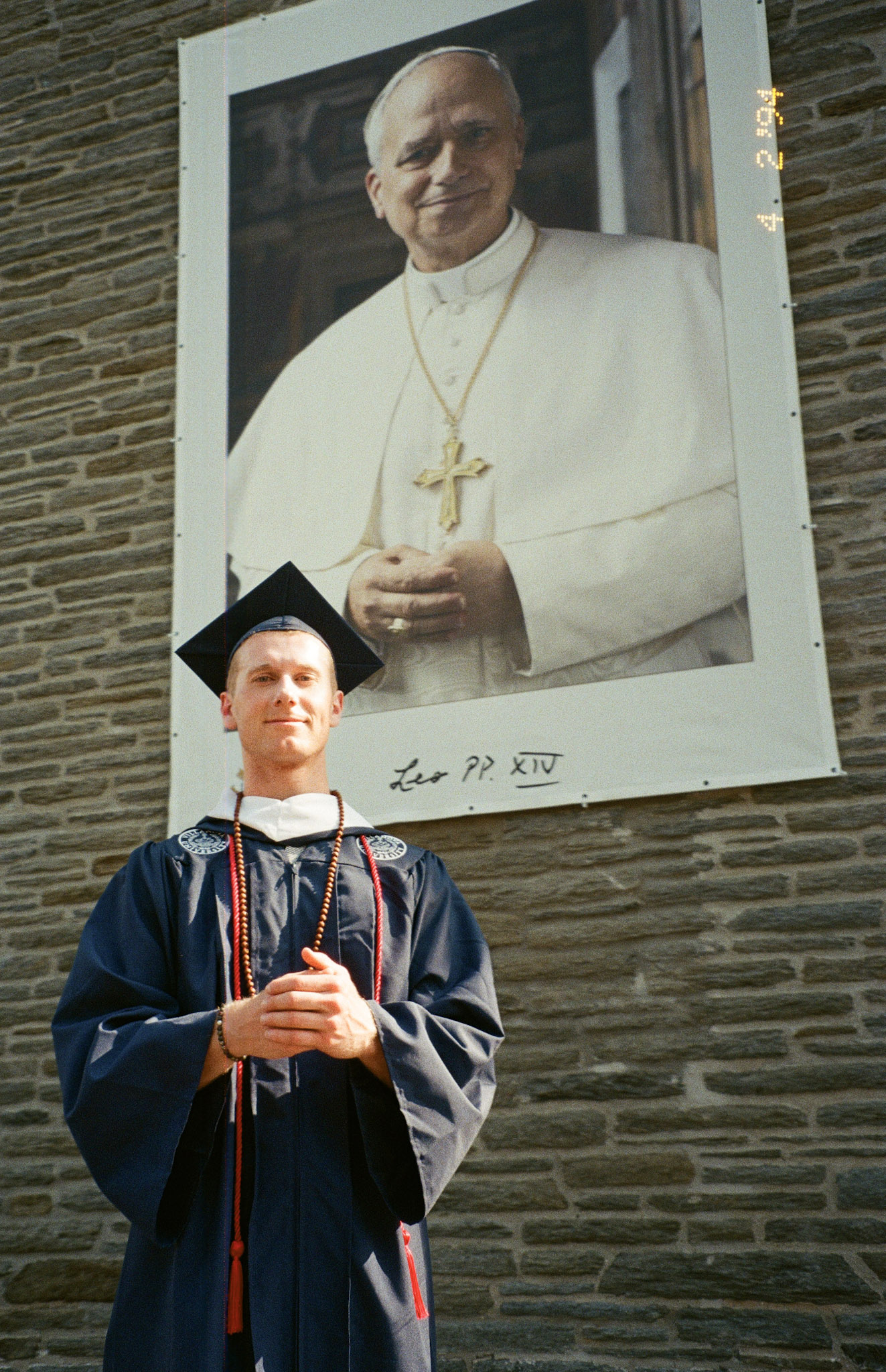 Graduate standing beneath a Pope portrait