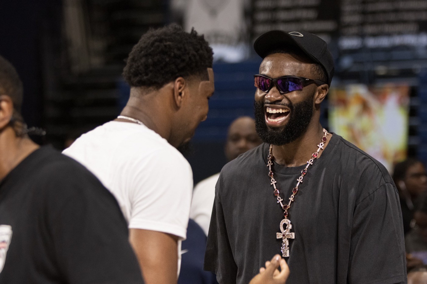 Jaylen Brown laughing courtside while wearing sunglasses and a statement necklace