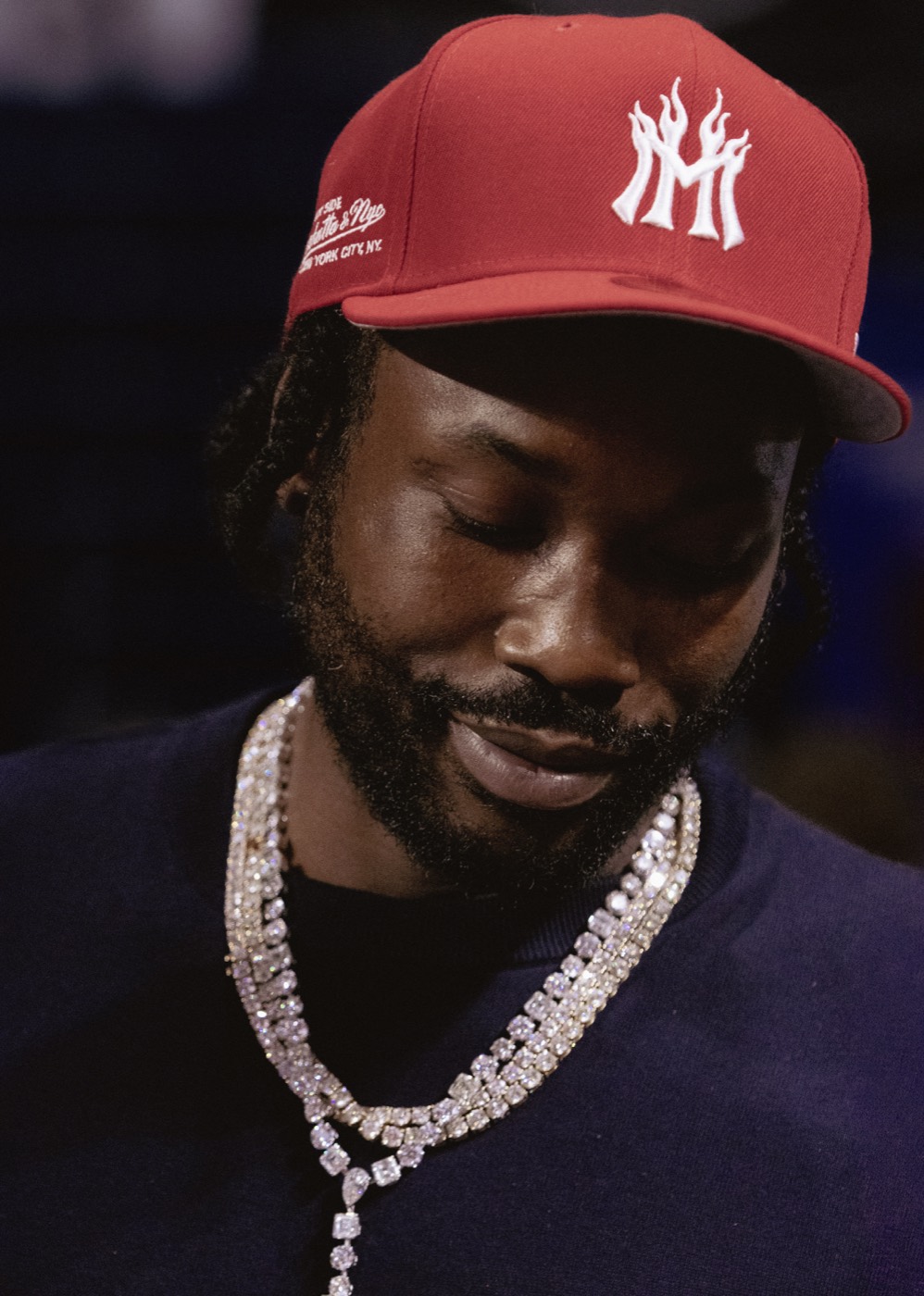 Meek Mill courtside portrait wearing a red cap and diamond necklace