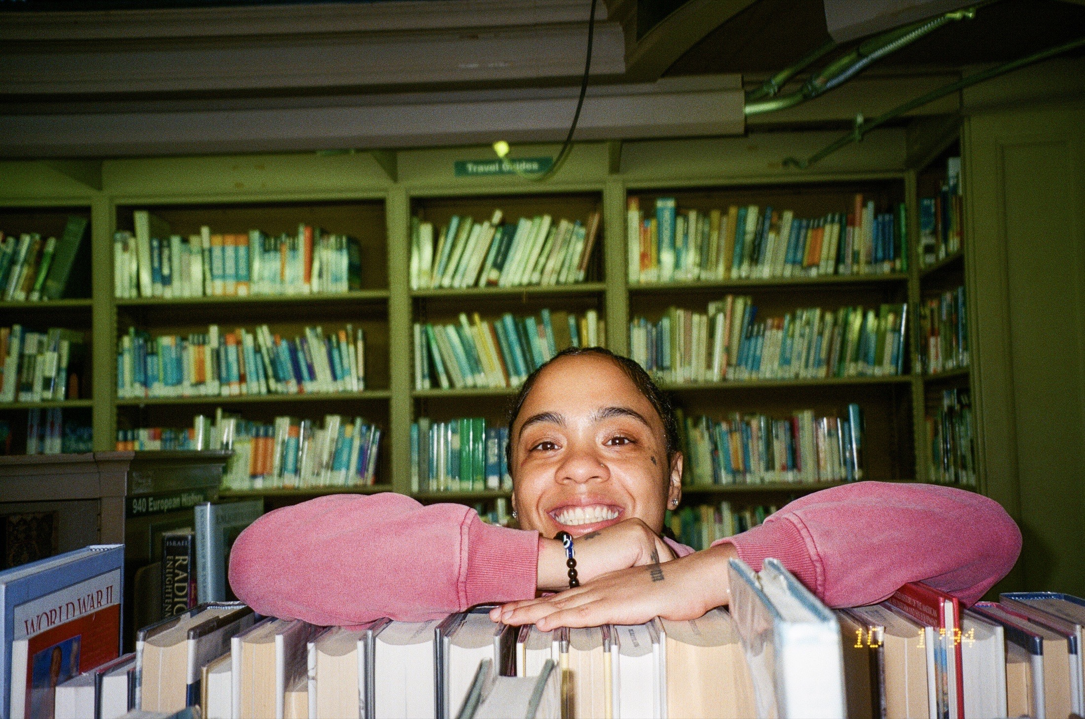 Fith and Saint pink sweatshirt portrait behind books