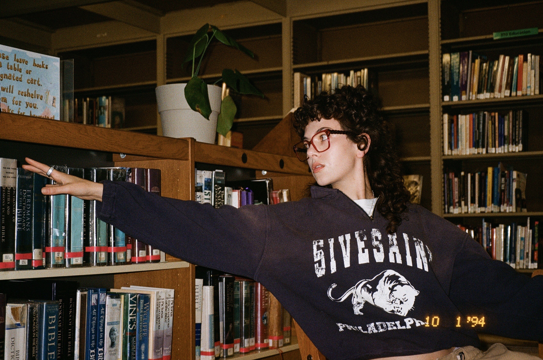 Fith and Saint model reaching across a bookshelf